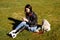 Young woman student with prosthetic leg sitting on green grass in university campus and using smartphone. Disabled woman