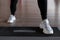 Young woman in stylish white sneakers in black leggings does exercises on the steps of the platform in the gym.