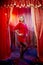 Young woman during a stylized theatrical circus photo shoot in a beautiful red location. Girl posing on stage with