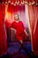 Young woman during a stylized theatrical circus photo shoot in a beautiful red location. Girl posing on stage with