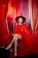 Young woman during a stylized theatrical circus photo shoot in a beautiful red location. Girl posing on stage with