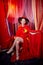 Young woman during a stylized theatrical circus photo shoot in a beautiful red location. Girl posing on stage with