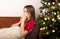 Young woman suffering from flu or coronavirus at christmas. Lying on sofa near decorated fir tree and sneezing and blowing her