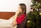 Young woman suffering from flu or coronavirus at christmas. Lying on sofa near decorated fir tree and sneezing and blowing her