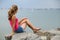 Young woman in summer clothes sitting on big boulders on sea shore looking on horizon