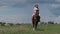 Young Woman in Summer Dress and Hat Riding Horse in Rural Field, Slow Motion