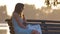 Young woman in summer dress sitting relaxed on lake side bench on warm evening. Wellness resting from everyday rush