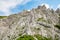 Young woman summer hiker with backpack climbing with help of metal cables, iron rungs, pegs, and steps on huge limestone rock wall