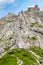 Young woman summer hiker with backpack climbing with help of metal cables, iron rungs, pegs, and steps on huge limestone rock wall