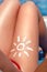 Young woman with sun shape on the leg holding sun cream bottle on the beach. Sun protection sun cream, on her smooth tanned legs.