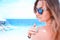 Young woman with sunglasses applyng sun protector cream at her hand on the beach close to tropical turquoise sea under blue sky