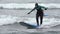 Young woman surfer in hooded wetsuit rides wave in Pacific Ocean on Kamchatka. Slow motion shot