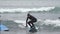 Young woman surfer in hooded wetsuit rides wave in Pacific Ocean on Kamchatka. Slow motion shot