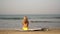 Young woman surfer sitting on a sandy beach on a surfboard