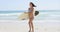 Young woman surfer striding along a tropical beach