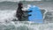 Young woman surfer in wetsuit pulling surfboard walking chest deep in splashing breaking waves of Pacific Ocean to go