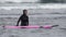 Young woman surfer in wetsuit pushes surfboard going waist deep in water of waves of Pacific Ocean. Slow motion