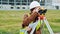 Young woman surveyor in green work clothes and helmet adjusts the equipment, produces calculations and writes to the