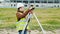 A young woman surveyor in work clothes and helmet adjusts the equipment and produces calculations on the construction