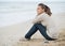 Young woman in sweater with cell phone sitting on lonely beach