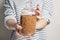 Young woman in sweater holding buckwheat in glass jar for storage against a white wall