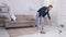 Young woman sweeping floor at home, using broom and scoop, slow motion