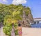 Young woman in swimsuit from behind in front of a palm tree on the sandy beach Naminoue topped by a huge rock with a Shinto Shrine