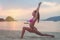 Young woman in swimsuit exercising on beach stretching her legs during sunset at sea. Fitness girl doing exercises on