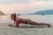 Young woman in swimsuit exercising on beach stretching her legs during sunset at sea. Fitness girl doing exercises on