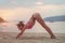 Young woman in swimsuit exercising on beach stretching her legs during sunset at sea. Fitness girl doing exercises on