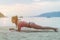 Young woman in swimsuit exercising on beach stretching her legs during sunset at sea. Fitness girl doing exercises on