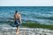 Young woman in a swimsuit and pareo walks into the sea - view from the back. Real adult girl on a background of blue water with