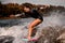 Young woman in swimsuit riding wave on surf style wakeboard and lifting up lot of splashes