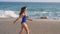 Young woman in swimsuit running on sea beach. Girl jogging along ocean shore. Female tourist having fun. Concept of