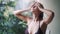 Young woman in swimsuit takes rain shower, tropical greenery on background