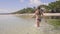 Young woman in swimsuit walking on transparent sea water on tropical beach. Happy woman enjoying clear water on ocean