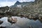 Young woman in swimsuit, warm hat sitting on the rock in the middle of the cold mountain lake, rocky ranges and stones