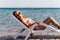 Young woman in a swimsuit wearing sunglasses lies on a deckchair
