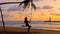 Young woman swinging sitting on rope swing suspended from palm tree at sea beach in sunset lights. Girl silhouette enjoy