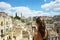 Young woman take photo with mirrorless camera to the old town of Matera. Beautiful traveller girl visit Sassi di Matera. Typical i