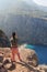 Young woman taking pictures on smartphone at Butterfly Valley from above, sitting on the rocks. Landscape Oludeniz, Turkey