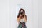 Young woman taking a self portrait in the mirror at home. White walls and background. Reflex camera covering her face. Lifestyle