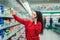 A young woman is talking on the phone and choosing products in a supermarket. Side view. The concept of consumption and modern