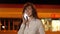 Young woman talking on the smartphone in parking lot at night by light of lanterns. Beautiful girl talking on phone at