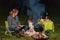 Young woman talks to her Australian Shepherd outside by a campfire. At dusk. Bread, cheese and wine on the table