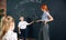 Young woman, teacher standing by blackboard with little boy, child and teaching math at school. Solving geometry tasks