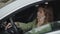 A young woman is tensely talking on the phone while behind the wheel of a car