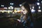 Young woman texting cell phone in city at night on bokeh