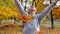 Young woman throwing golden maple leaves with joyful mood at autumn park. Happy girl playing with lush foliage at