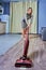 Young woman in a tight dress vacuums the floor